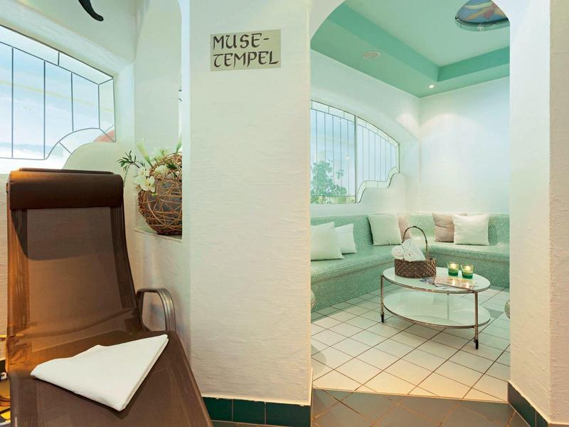 Gemütlicher Innenraum mit weiß-grünen Wänden, Eckbank, rundem Tisch und braunem Liegestuhl.