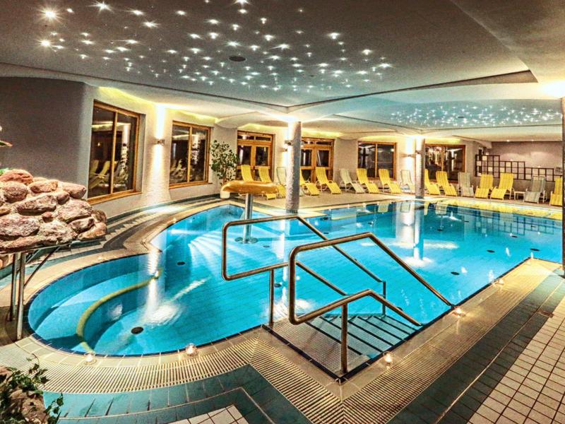 Innenpool mit blauen Fliesen, Treppen, Lichtern an der Decke und Liegestühlen im Hintergrund.