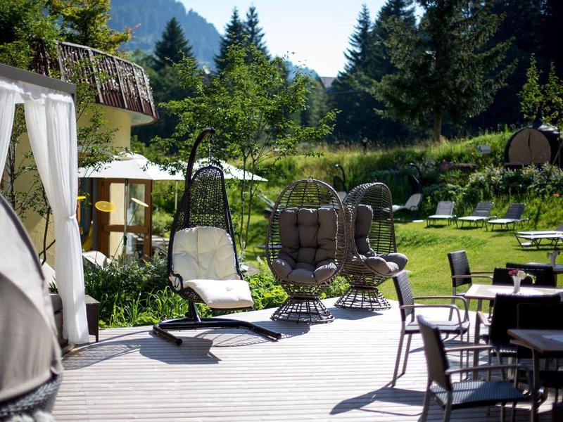 Sonnige Terrasse mit Stühlen, Schaukelsesseln und gepflegtem Garten im Hintergrund.