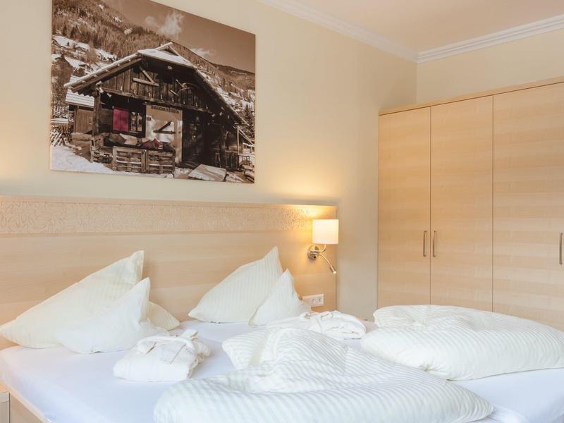 Schlichtes Schlafzimmer mit weißer Bettwäsche, Holzmöbeln und Winterlandschaftsfoto an der Wand.