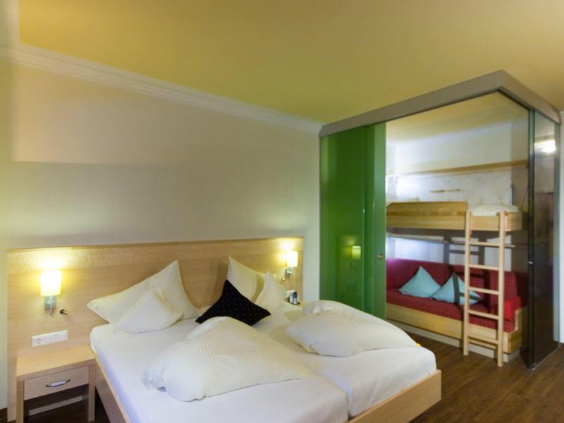 Modernes Hotelzimmer mit Doppelbett, Stockbett, grüner Glasscheibe und Holzboden.