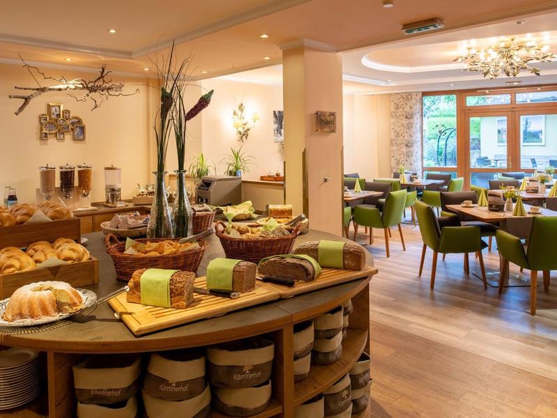 Gemütlicher Frühstücksraum mit Holzmöbeln, frischem Gebäck und grünen Stühlen, hell und einladend.