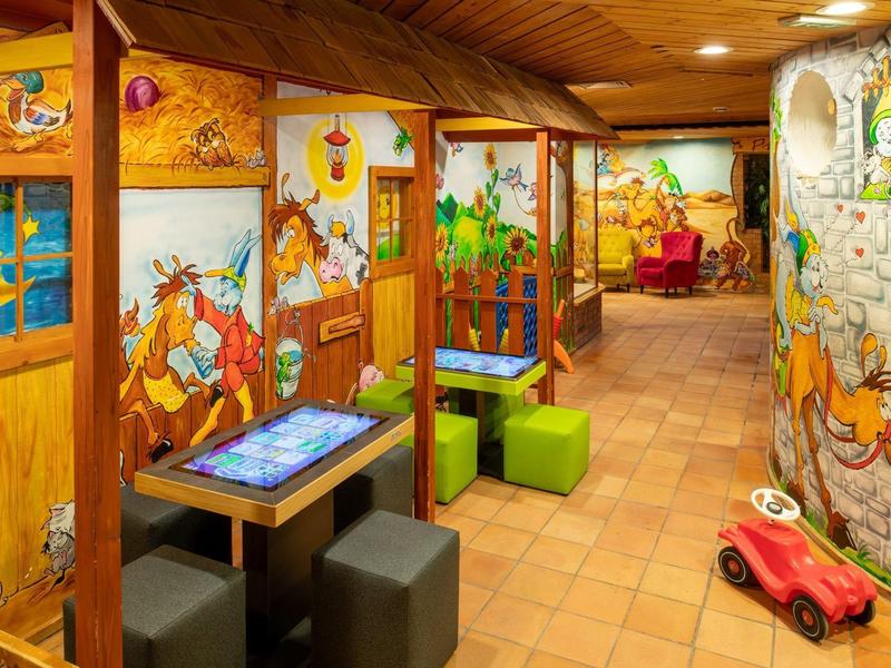 Bunt gestalteter Kinderbereich mit Holzwänden, Sitzwürfeln, Tischen und kleinem roten Spielauto.