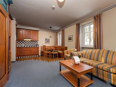 Gemütliches Wohnzimmer mit gestreiftem Sofa, Holztisch, Esstisch und Küchenzeile in warmen Tönen.