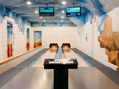 Moderne Indoor-Bowlingbahn mit bemalten Wänden und Decke, zwei Monitoren und zwei Bahnen.