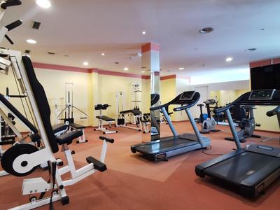 Hell erleuchteter Fitnessraum mit verschiedenen Trainingsgeräten und roten Teppichboden.