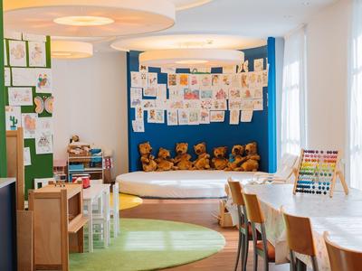 Ein heller, freundlicher Klassenraum mit Teddybären, Kinderzeichnungen und buntem Spielzeug.