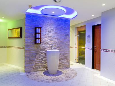 Moderner Raum mit rundem Steinsockel, beleuchtetem Deckenelement und zwei Türen rechts.