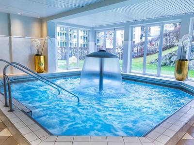 Moderner Innenpool mit Wasserfontäne, großen Fenstern und goldfarbenen Pflanzgefäßen.