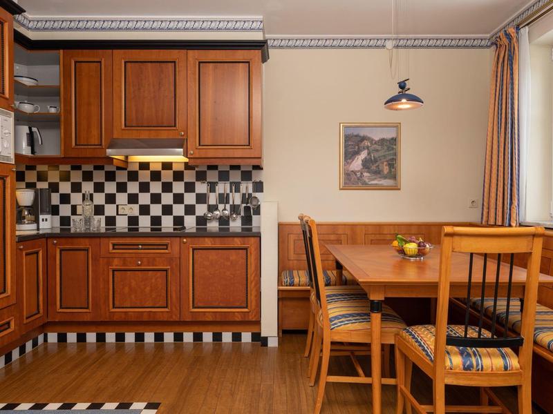 Küche mit Holzschränken, schwarz-weiß gekachelter Rückwand und Holztisch mit Stühlen am Fenster.