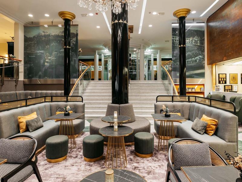 Elegantes Hotel-Lobby mit grauen Sofas, goldenen Akzenten, Teppichboden und Kronleuchter.