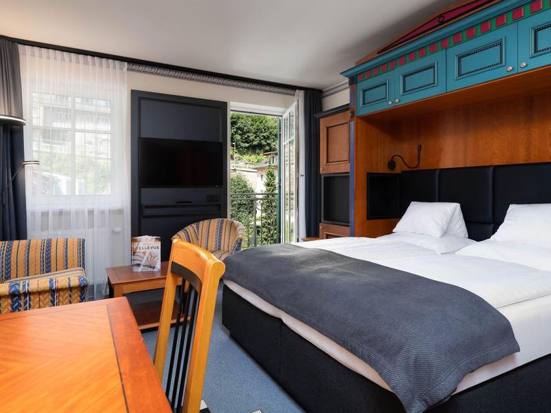 Modernes Hotelzimmer mit Doppelbett, Schreibtisch, Stuhl, Sesseln und Balkon mit Blick ins Grüne.