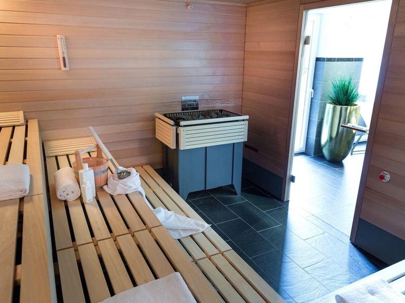 Helle Sauna mit Holzbänken, Handtüchern und Schieferboden, daneben Tür mit Blick auf Pflanzen.