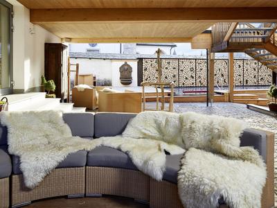 Salon extérieur confortable avec canapé gris, couvertures duveteuses et terrasse sur le toit en bois.