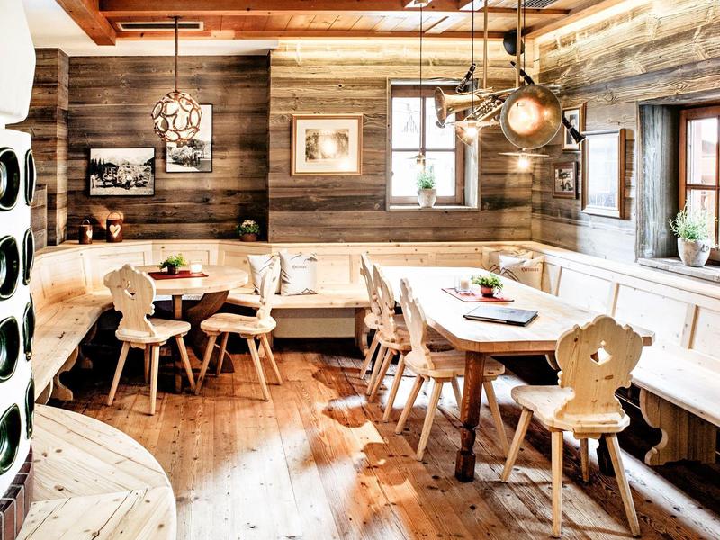 Coin repas rustique avec mobilier en bois, coussins blancs et lambris en bois chaleureux aux murs.