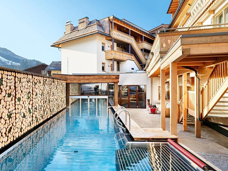 Piscine sur la terrasse d'un hôtel de montagne avec revêtement en bois et vue sur les montagnes.
