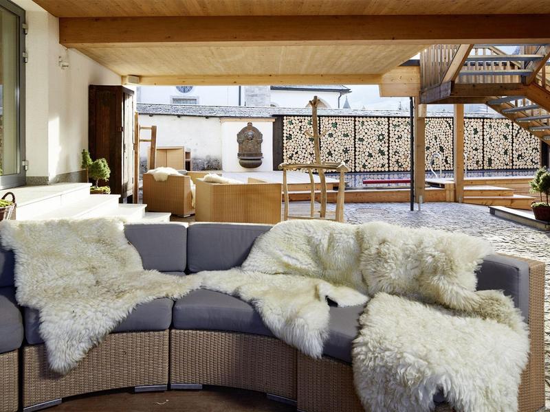 Salon extérieur confortable avec canapé gris, couvertures duveteuses et terrasse sur le toit en bois.