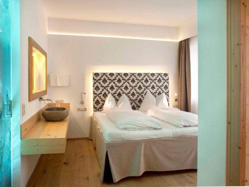 Chambre d'hôtel lumineuse avec lit double, tête de lit à motifs, sol en bois et éclairage doux.