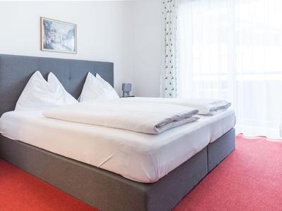 Chambre lumineuse aménagée avec grand lit et tapis rouge.