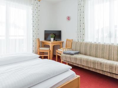 Chambre d'hôtel lumineuse avec lit double, canapé, petite table et télévision devant des rideaux à la fenêtre.
