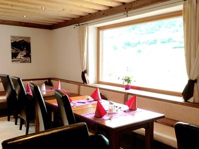 Restaurant lumineux avec table en bois, chaises noires, serviettes rouges et grande fenêtre.