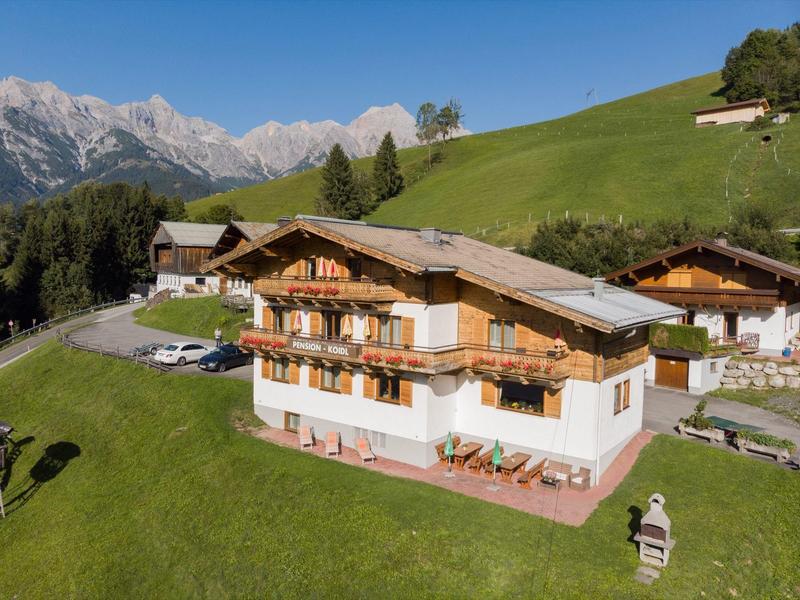 Mountain hotel with wooden balconies and green meadow against mountain backdrop