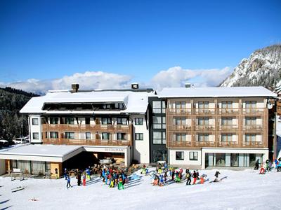 Velká hotelová budova v zasněžené horské krajině s mnoha lidmi před ní.