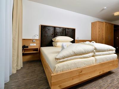 Jednoduchý hotelový pokoj se dřevěnou postelí, čelem postele, měkkou přikrývkou a polštáři.