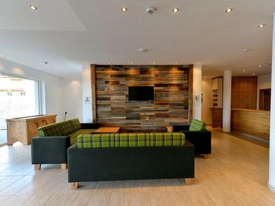 Modern hotel lounge area with sofa, TV, and wooden wall paneling.