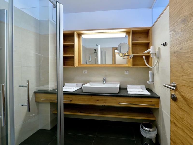 Moderní koupelna se dvěma umyvadly, dřevěnými policemi a skleněnými dveřmi do sprchy.