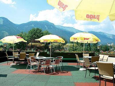 Dachterrasse mit Tischen, Stühlen und gelben Sonnenschirmen, Bergen und blauem Himmel im Hintergrund.
