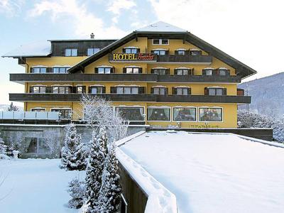 Hotel met gele gevel in besneeuwd winterlandschap en bergen op de achtergrond.