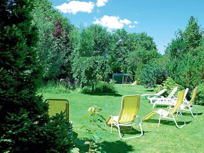 Groene tuin met ligstoelen voor bomen onder een blauwe lucht.