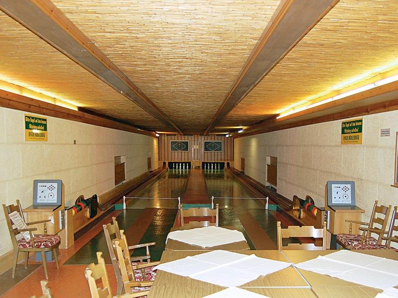 Interieur van een bowlingbaan met tafels en stoelen, heldere verlichting en houten vloer.