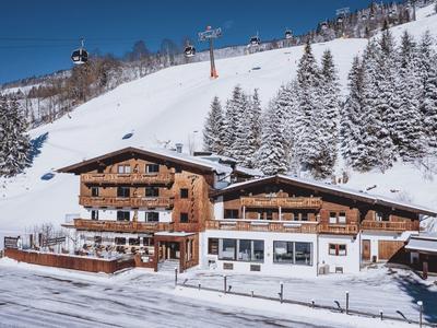 Rustic wooden mountain hotel next to a snow-covered slope with ski lifts and snow-covered fir trees.