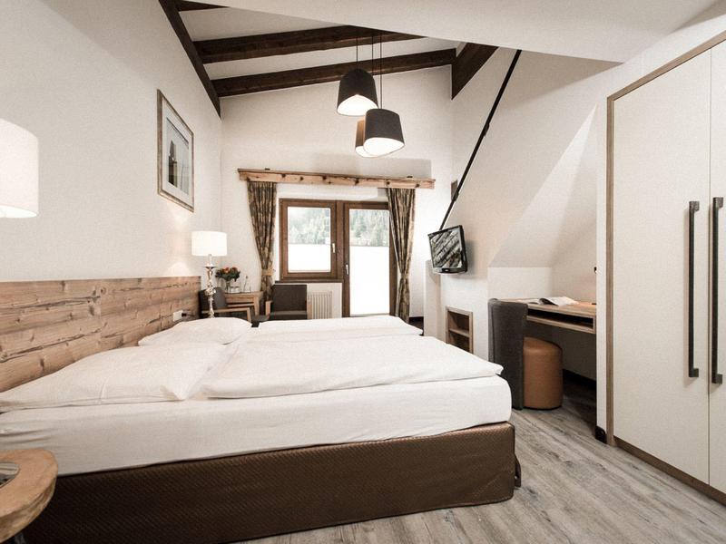 Bright hotel room with wood accents, large bed, desk, and TV on slanted wall.