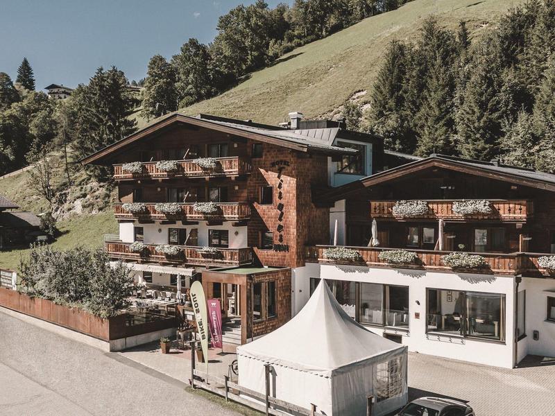 Cozy hotel building with balconies and flowers in a green mountain landscape.