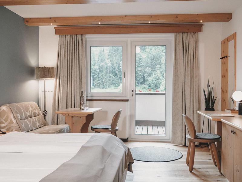 Cozy hotel room with double bed, desk, and glass door leading to balcony.