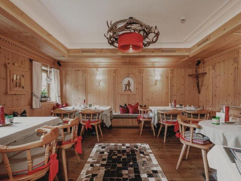 Rustic dining room with wooden furniture, white tablecloths, and a deer antler chandelier on the ceiling.