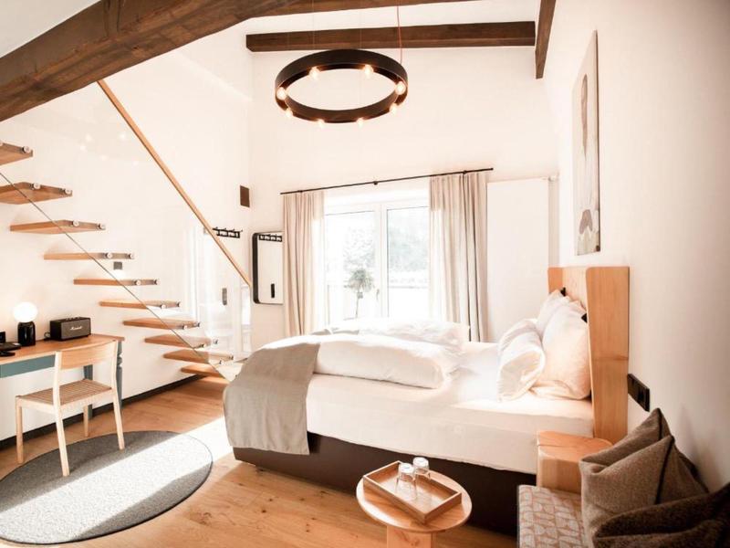 Bright hotel room with wooden staircase, large window, and cozy bed with white bedding.