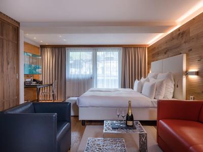 Przytulny pokój hotelowy z łóżkiem podwójnym, czerwono-niebieską sofą i butelką szampana na stole.