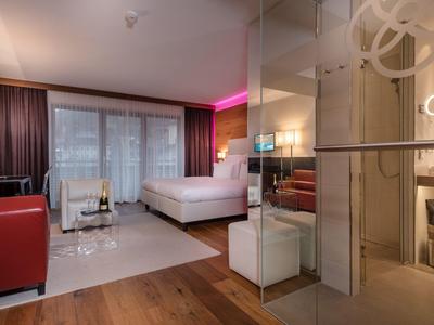 Nowoczesny pokój hotelowy z łóżkiem podwójnym, szklaną prysznicem i częścią wypoczynkową z sofą.