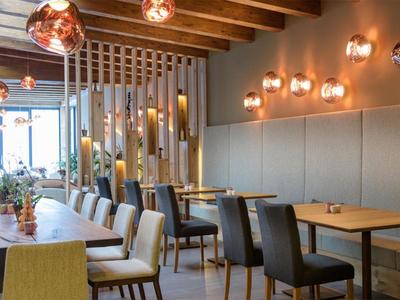 Modern restaurant with wooden beam ceiling, comfortable chairs, and warm wall lamps.