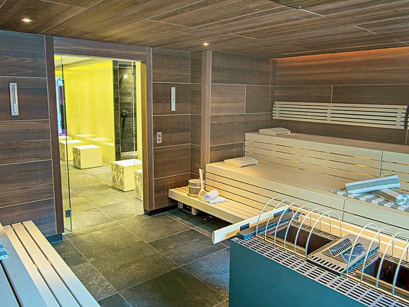 Nowoczesna sauna z drewnianymi ławkami i przylegającą strefą relaksu z żółtym światłem.