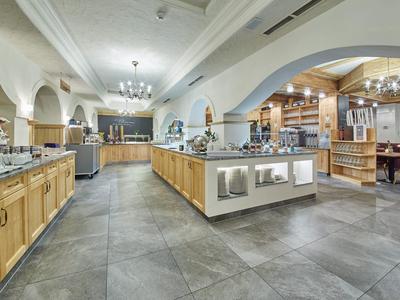 Prostorná hotelová kuchyně s moderními spotřebiči, dřevěnými skříněmi a šedou dlažbou.