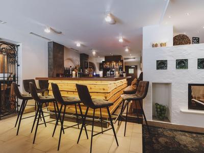 Área de bar moderna en hotel con mostrador de madera, taburetes altos y chimenea en un entorno elegante.