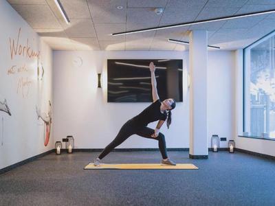 Mujer haciendo yoga en colchoneta en sala de fitness moderna y luminosa con grandes ventanas.