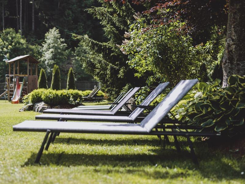 Několik lehátek je umístěno na udržované trávě vedle keřů a stromů.