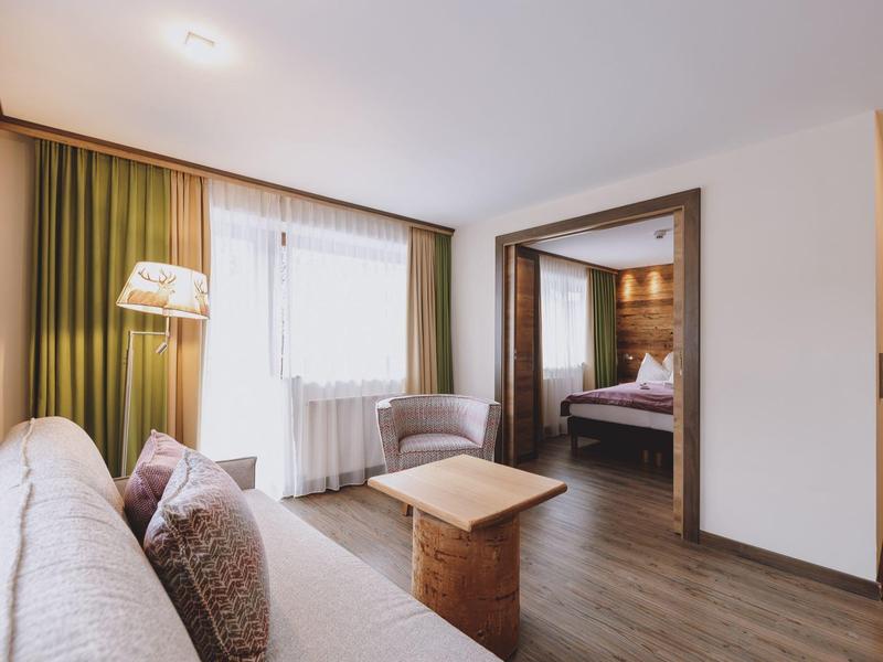 Pohodlný hotelový pokoj s pohovkou, křeslem, stolem a výhledem do ložnice.