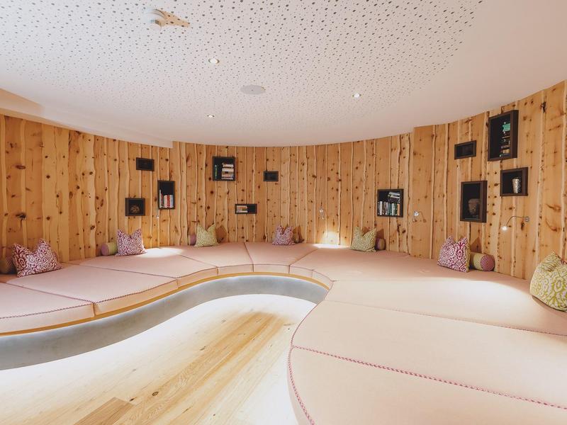 Pohodlná relaxační místnost ve spa s zakřiveným dřevěným interiérem a měkkými polštáři na sezení.